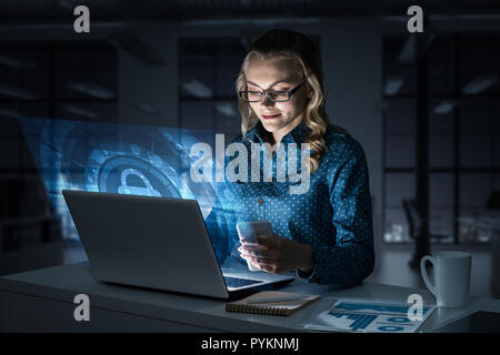Belle blonde bureau sombre en travaillant sur ordinateur portable et obtenir sw Banque D'Images