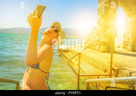 Happy tourist bikini femme prend au coucher du soleil en selfies piscine naturelle de Nauplie, Péloponnèse, Grèce, Europe. Femme avec smart phone en voyage de vie. Banque D'Images