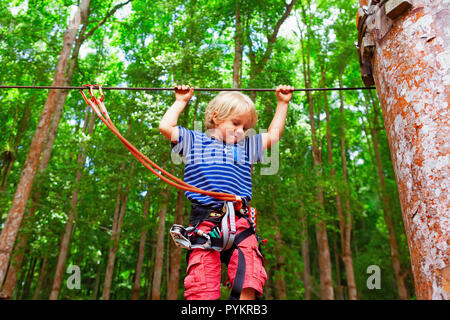 Enfant en harnais, bourrelets de protection fixée par mousquetons pour fil. Grimper sur le tree top, col pont suspendu au parc aventure. Banque D'Images