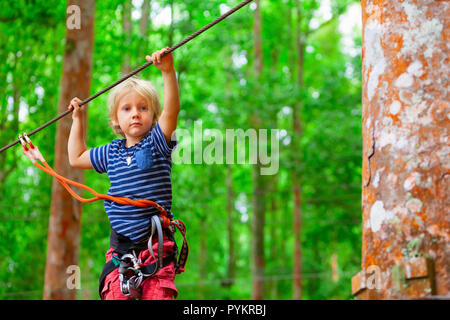 Enfant en harnais, bourrelets de protection fixée par mousquetons pour fil. Grimper sur le tree top, col pont suspendu au parc aventure. Banque D'Images