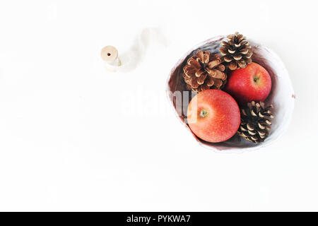 Fruits pomme rouge et des pommes de pin en céramique bol et ruban de soie sur fond de table blanc. Style de vacances de Noël stock photo. La composition des aliments d'hiver. Mise à plat, vue du dessus. Banque D'Images