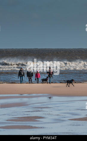 Une famille et leurs deux chiens labrador noire sur la plage de Blackpool, Lancashire par une froide journée d'hiver venteux en plein soleil et une mer agitée Banque D'Images