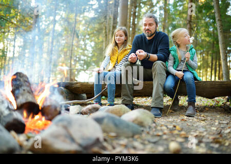 Jolie petite soeurs et leur père les guimauves grillées sur des bâtons à feu. Les enfants s'amuser au feu de camp. Camping avec les enfants dans la forêt de l'automne. F Banque D'Images