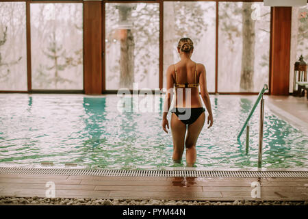 Jolie jeune femme d'entrer dans l'eau à une piscine dans le centre de spa Banque D'Images