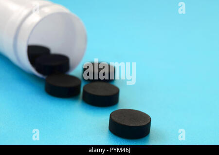Plusieurs tablettes Noir tomber du pot en plastique sur la surface bleue. Image de fond sur des sujets médicaux et pharmaceutiques. Le charbon activé Banque D'Images