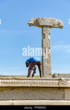 Un jardinier travaille à côté d'une colonne en pierre qui faisait autrefois partie du marché complexe ; ce qui est aujourd'hui en ruine près du Vijaya Vitthala Temple, Hampi. Banque D'Images