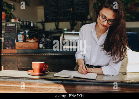 Happy young woman sitting in the cafe à écrire des notes dans son journal. Les femmes prennent des notes dans son livre tout en vous relaxant au coffee shop. Banque D'Images