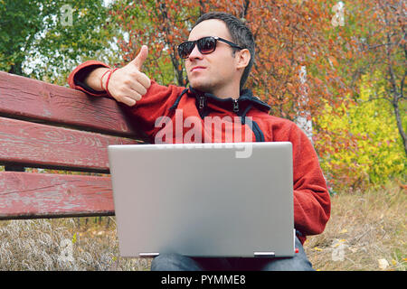 Un homme lit des messages, des informations sur l'Ultrabook et montre un doigt vers le haut. C'est très bien. Heureux jeune homme ou homme hipster en vêtements décontractés vous détendre assis sur Banque D'Images