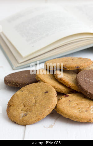 Des biscuits fraîchement cuits mélangés sur une table rustique en bois blanc avec un livre ouvert. Banque D'Images