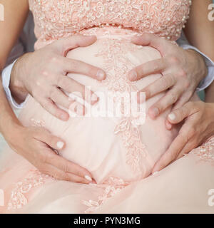 Femme enceinte en robe rose détient les mains sur le ventre. La grossesse, la maternité, la préparation et l'attente concept. Close-up, à l'intérieur. Belle grossesse. Banque D'Images