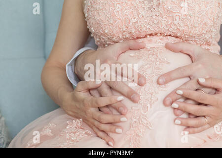 La grossesse, la maternité, la préparation et l'attente concept. Homme et femme enceinte en robe rose détient les mains sur le ventre. Banque D'Images