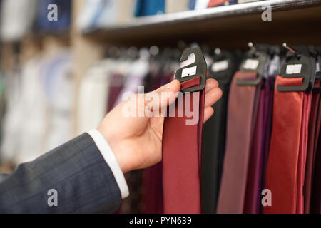 Récolte de la main de l'homme tenue cravate bordo dans une boutique. Magasin de mode masculine accesorize colorée et élégante sur des cintres. Le choix parfait pour l'élément client nouveau look. Concept de mode et de style. Banque D'Images