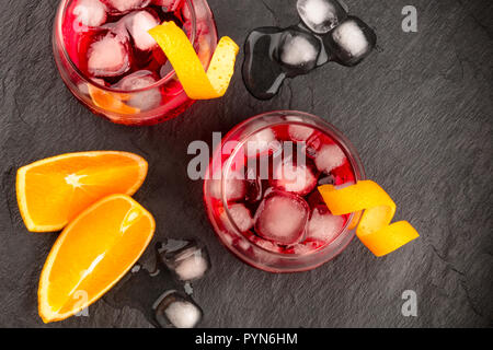 Deux cocktails avec campari Negroni dynamique et tordu le zeste d'orange garnitures, tourné à partir du haut, avec des cubes de glace et les tranches de fruits sur un fond noir, avec une place pour le texte Banque D'Images