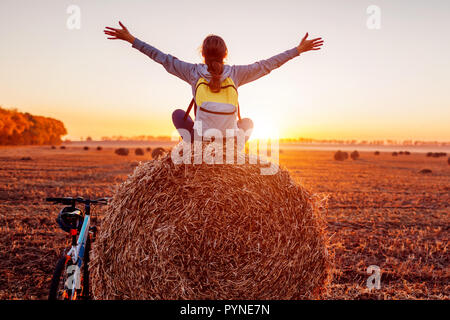 Les jeunes cyclistes assis sur botte avec soulevées et bras ouverts après un tour. Femme qui reste dans le champ d'automne admirant la vue. Vie Sportive Banque D'Images