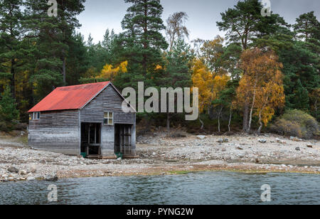 Un hangar au toit rouge sur les rives du Loch Vaa dans les Highlands écossais, prises au cours de l'automne avec les arbres montrant leurs couleurs vives. Banque D'Images