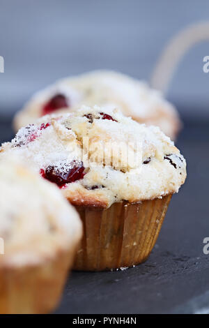 Muffins aux canneberges avec sucre citron garniture sur une ardoise rustique servant des bac. l'extrême profondeur de champ avec l'accent sur le centre de muffin. Banque D'Images