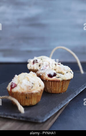 Muffins aux canneberges avec sucre citron garniture sur une ardoise rustique servant des bac. l'extrême profondeur de champ avec l'accent sur le centre de muffin. Banque D'Images