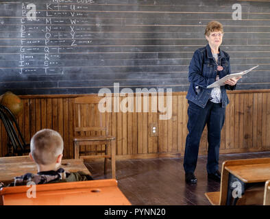 Teacher holding parle à livre ouvert school boy à vintage bureau en bois. Tableau noir avec des lignes blanches derrière. Wilmeth Schoolhouse, McKinney au Texas. Banque D'Images