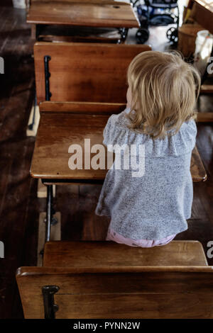 Fille de l'école dans une robe vintage se trouve au bureau en bois en classe. Wilmeth Schoolhouse, Chestnut Square Village historique, McKinney au Texas. portrait Banque D'Images