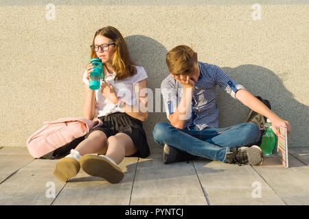 Les écoliers adolescents fatigués s'asseoir près du mur gris de l'école. Banque D'Images