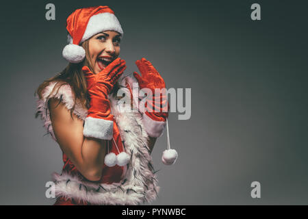 Portrait d'une belle jeune femme en costume de Père Noël s'amusant et étonné à à huis clos. Banque D'Images