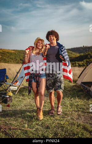 Happy young couple bénéficie d'une journée ensoleillée dans la nature. Ils êtes serrant les uns les autres, enveloppés dans le drapeau américain. Banque D'Images