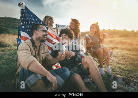 Happy friends Celebrating Independence Day et profitez d'une journée ensoleillée à la montagne. Ils êtes holding american flag, rire et toasting with beer Banque D'Images