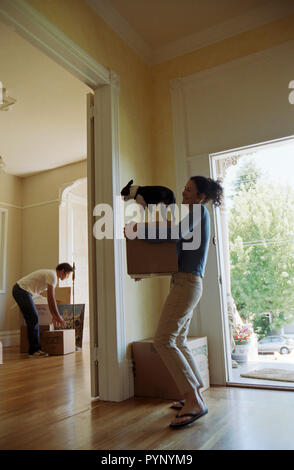 Happy young woman carrying a fort avec son petit chien au-dessus d'elle dans sa nouvelle maison. Banque D'Images