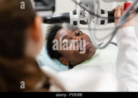 Young African American male patient au fauteuil à une clinique dentaire. La médecine, de la santé, concept stomatologie dentiste procède à l'inspection et. conclut Banque D'Images