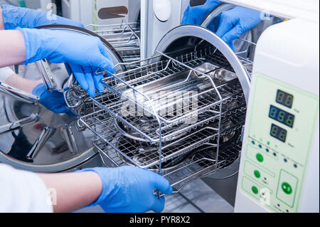 Les mains de l'assistant dentiste sortir la stérilisation des instruments médicaux d'autoclave. Focus sélectif. Banque D'Images