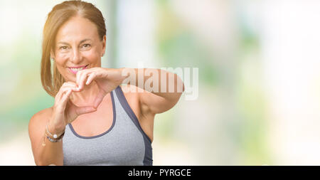 Belle femme d'âge moyen portant des vêtements de sport sur fond isolé smiling in love montrant le symbole de coeur et la forme des mains. Concept romantique. Banque D'Images