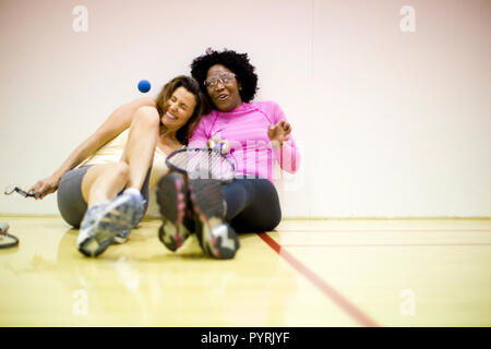 Deux femmes souriant assis ensemble sur un terrain de racquetball. Banque D'Images