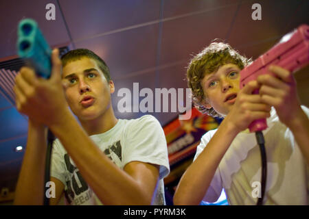 Deux adolescents jouant un jeu vidéo de tir à l'intérieur d'une arcade de jeux. Banque D'Images