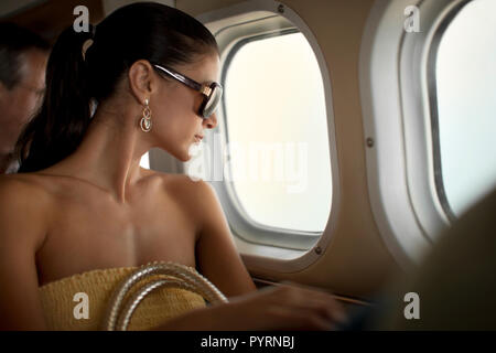 Jeune femme contenu regarder hors d'une fenêtre de l'avion. Banque D'Images