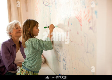 Femme mature montres joyeusement sa jeune petite-fille d'écrire sur un mur avec une peinture murale chambre feutre. Banque D'Images