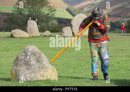 New-age man blowing un didgeridoo vers les pierres du cercle de pierres de Castlerigg dans le Lake District, Cumbria, Angleterre Banque D'Images