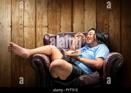 Asian fat man eating donuts sur la plaque dans le canapé. Fat Man concept de régime Banque D'Images