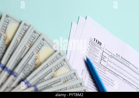1120 formulaire d'impôt se trouve près de cent dollars et stylo bleu sur un fond bleu clair. Nous joindre - Déclaration de revenus des sociétés. Banque D'Images