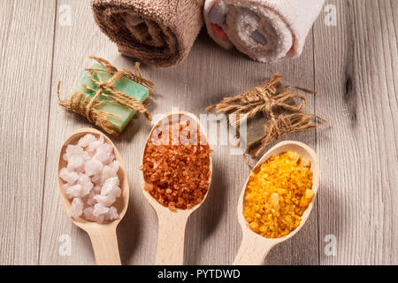 Wooden spoons with white, yellow and brown sea salt and handmade soap for bathroom procedures with towels on the background. Spa products and accessor Banque D'Images