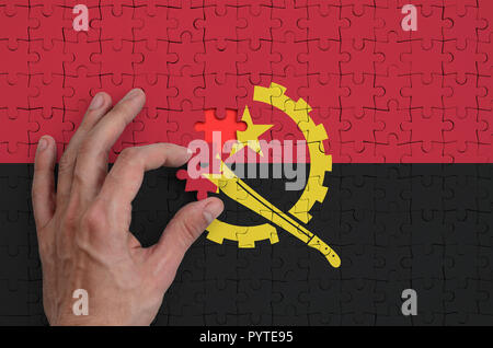 Drapeau de l'Angola est représenté sur un casse-tête, qui la main de l'homme achève de se plier. Banque D'Images