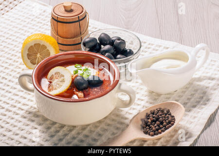 Saltwort soupe à la viande, saucisses fumées, pommes de terre, tomates, concombre mariné mariné, citron, olives noires et la crème sure dans un bol à soupe en céramique avec Banque D'Images