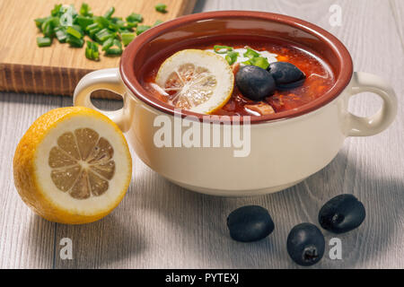 Saltwort soupe à la viande, saucisses fumées, pommes de terre, tomates, concombre mariné mariné, citron, olives noires et la crème sure dans un bol à soupe en céramique avec Banque D'Images