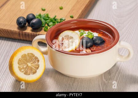 Saltwort soupe à la viande, saucisses fumées, pommes de terre, tomates, concombre mariné mariné, citron, olives noires et la crème sure dans un bol à soupe en céramique avec Banque D'Images