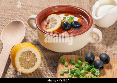 Saltwort soupe à la viande, saucisses fumées, pommes de terre, tomates, concombre mariné mariné, citron, olives noires et la crème sure dans un bol à soupe en céramique avec Banque D'Images