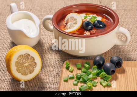 Saltwort soupe à la viande, saucisses fumées, pommes de terre, tomates, concombre mariné mariné, citron, olives noires et la crème sure dans un bol à soupe en céramique avec Banque D'Images