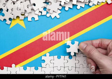 République démocratique du Congo drapeau est représenté sur une table sur laquelle la main de l'homme plie un puzzle de couleur blanche. Banque D'Images