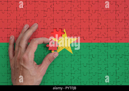 Drapeau du Burkina Faso est représenté sur un casse-tête, qui la main de l'homme achève de se plier. Banque D'Images