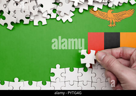 La Zambie drapeau est représenté sur une table sur laquelle la main de l'homme plie un puzzle de couleur blanche. Banque D'Images