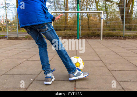 Boy kicking ball sur le terrain de soccer pavé urbain Banque D'Images