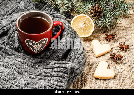 Tasse de thé rouge enveloppé dans l'écharpe de laine, tranche de citron, les branches de sapins avec cône, l'anis étoilé, cannelle et pain d'épices cookies au cœur sh Banque D'Images